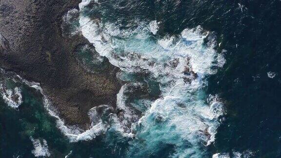 多岩石的海岸线对比泡沫波和绿松石水鸟瞰图