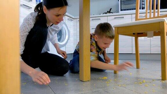 母亲责备儿子把食物撒在厨房地板上并要他把地板收拾干净一起清理地板上的玉米片