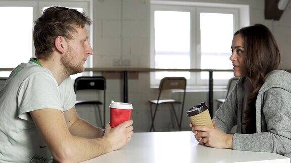 两个朋友坐在咖啡馆的桌边一边喝着纸杯外带的咖啡一边聊天在4k拍摄