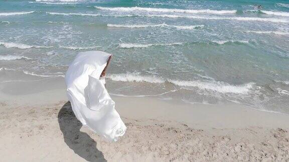 美丽的女人拿着织物在沙滩上