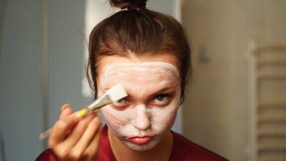 妇女用刷子将清洁面膜敷在脸上女性做面部皮肤护理程序女孩用护肤霜擦洗和滋润皮肤