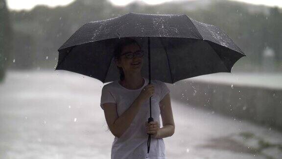 快乐的女孩在伞下享受着雨下着大雨慢动作在户外