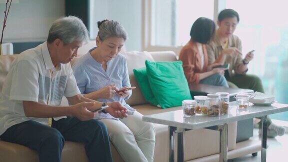 亚洲华人祖父母和年轻夫妇在客厅用手机浏览互联网