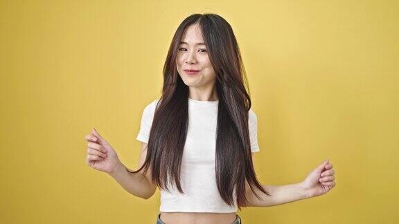 年轻的中国女子微笑着自信地在孤立的黄色背景上跳舞