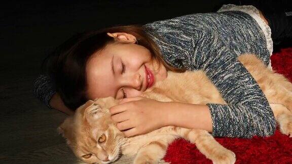 快乐的小女孩微笑拥抱和爱抚她的猫躺在家里的地板上的阳光