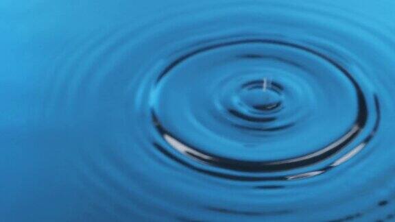 缓慢的运动两滴水滴落进蓝色、干净、冰冷的水中蓝色的水滴