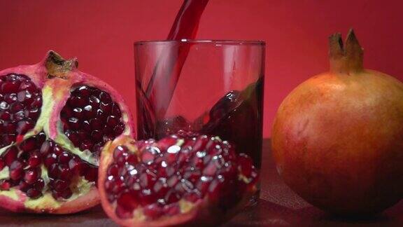 特写的红色果汁流进一个玻璃杯旁边的一半石榴