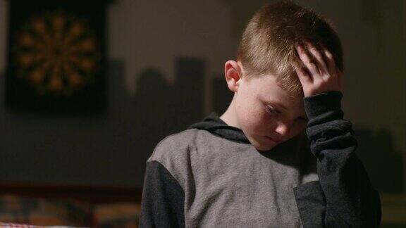 悲伤的小男孩独自站在自己的房间里双手抱头向下看