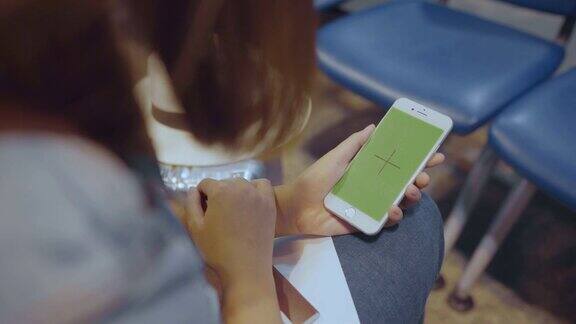 一名亚洲女子在国际机场使用绿色屏幕的白色手机