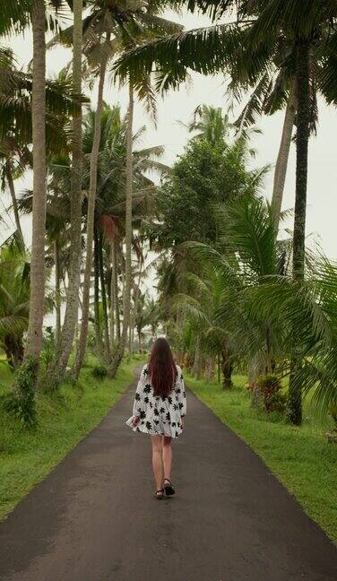 垂直视频中一个穿着裙子的年轻女孩在棕榈树中奔跑