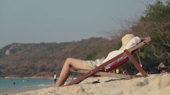 亚洲女性躺在沙滩上的躺椅上睡在沙滩上度假夏天的生活方式
