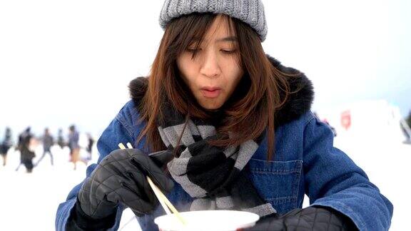 一个亚洲女人在雪冬吃方便面