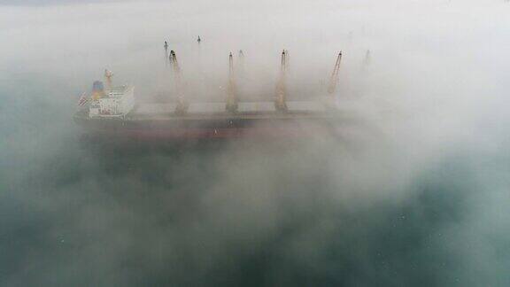 在保加利亚瓦尔纳海港无人机拍摄的大雾中的货船和工业起重机