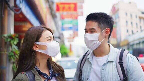 亚洲夫妇戴着面具在城市旅行度蜜月新婚男女背包客在疫情期间开心地一起享受假期然后看着镜头