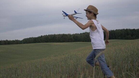 戴着草帽的快乐男孩梦想家手里拿着一架飞机跑过田野