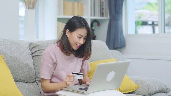 亚洲女性用笔记本电脑和信用卡购物电商女性坐在家里客厅的沙发上放松心情网上购物生活方式女性在家放松