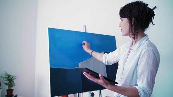 这位年轻的画家站在她的家庭工作室里直接在画布上从她的写字板上复制她的作品