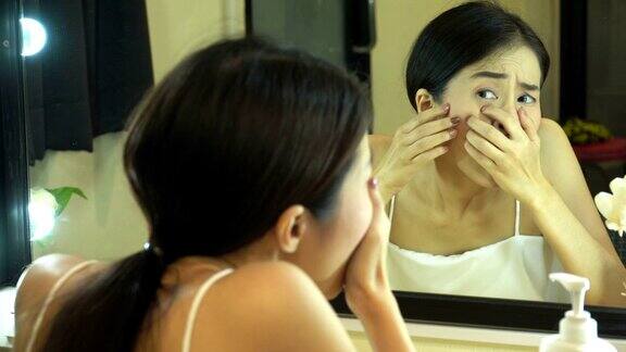 年轻的亚洲女孩与痤疮青少年女性照镜子和挤青春痘在浴室的肖像美容护肤的生活理念