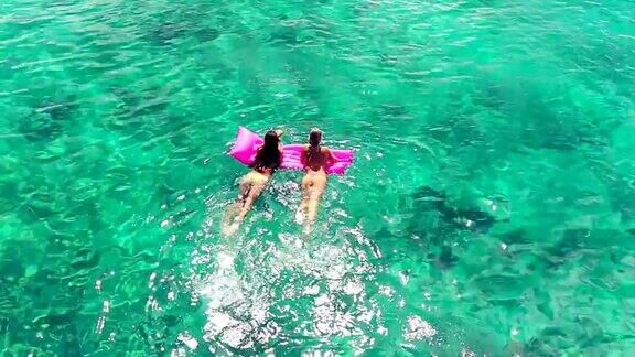 美丽的年轻女人穿着比基尼漂浮在粉红色的充气筏在水晶海洋在夏威夷