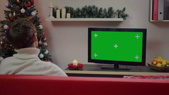 一名男子在圣诞装饰的客厅里看绿色屏幕模型电视