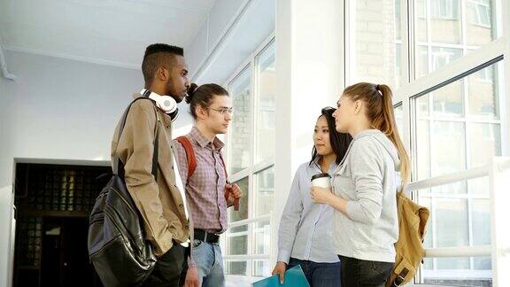 四个多民族的学生站在大学宽敞的白色大厅里积极地交谈他们正面地笑着大笑着