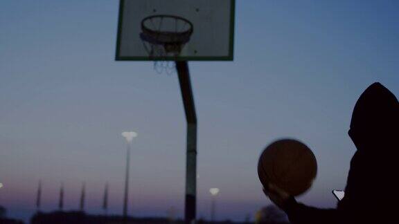 黄昏时分年轻人带着智能手机和篮球走出户外篮球场