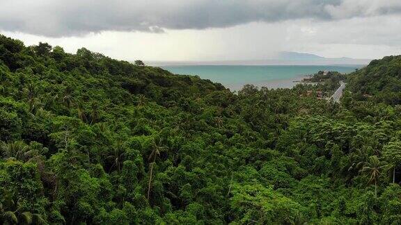 热带岛屿上空阴天灰色多云的天空绿色的棕榈树在泰国苏梅岛雨季无人机的观点飞越野生雨林和丛林附近的天堂海洋海滩风暴在亚洲