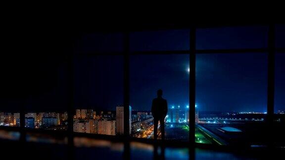 站在夜晚城市背景的窗边的男人时间流逝