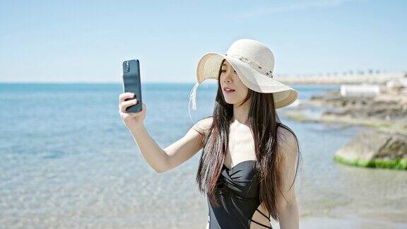 年轻的中国女游客穿着泳衣在海边用智能手机录视频