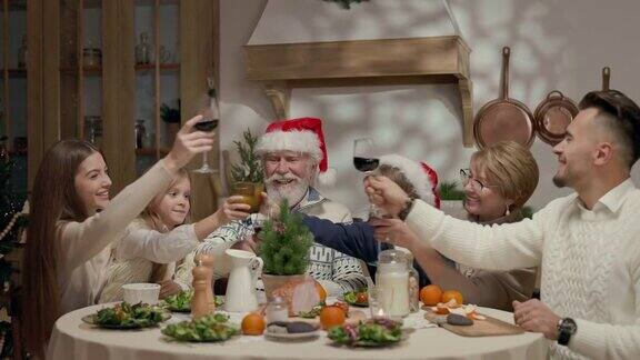 家庭年夜饭餐桌上一个戴圣诞帽的老人和一个戴眼镜的女人两个孩子一个男孩一个女孩两个年轻人他们打翻玻璃杯庆祝