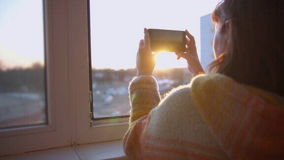 幸福的女人站在阳台上用手机拍摄日落