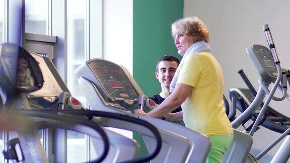 奶奶和教练在健身房的跑步机上训练