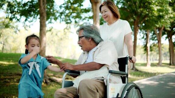亚洲一家在公园度假放松爷爷坐在轮椅上慢动作