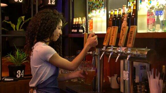 美丽的拉丁美洲女酒吧服务员提供啤酒然后面对镜头微笑