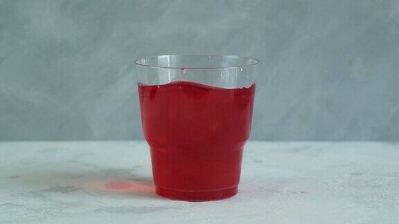 红色清爽饮料在塑料杯灰色背景水果冰茶五彩缤纷的夏日无酒精清凉饮料加冰块视频慢动作