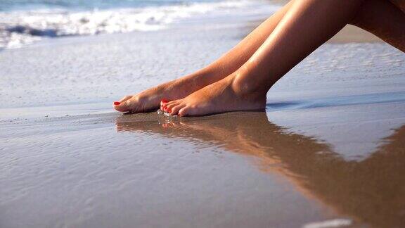 美丽的女性的腿躺在沙滩上放松在海边在阳光明媚的日子里一个面目全非的年轻女子坐在海边晒太阳度假胜地女孩的脚暑假或假日概念关闭侧视图慢动作