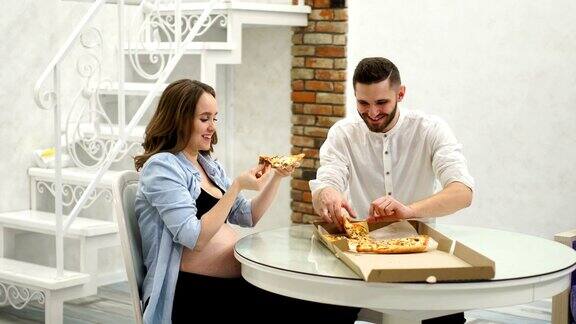 男人和孕妇在家厨房吃披萨高脂肪的食物