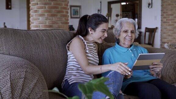 西班牙裔小孙女在家里教祖母使用数字平板电脑