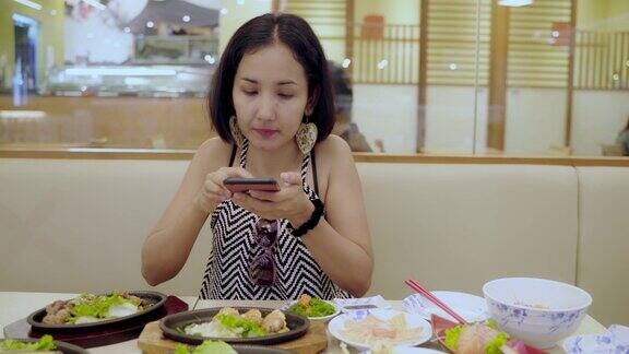 4K快乐年轻亚洲女性博主用智能手机拍摄新鲜的生鱼片、三文鱼日本食物并发布在社交网络上