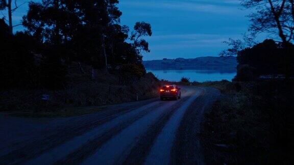 鸟瞰图汽车行驶在乡村道路上SUV驾驶在黄昏与前灯穿过松树