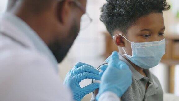 非裔美国男医生或护士在医院或家中为9岁儿童患者的肩部注射或接种疫苗同时接种疫苗和预防冠状病毒大流行COVID-19疫苗