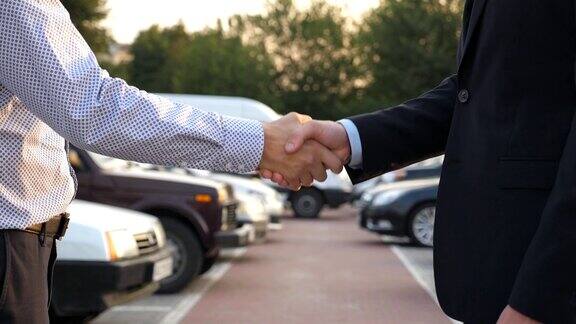 两个不认识的商人互相握手后面停着车经理或客户在室外握手伙伴们在外面握手特写慢动作侧视图
