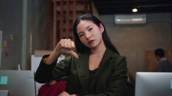 不高兴的亚洲女商人看着相机和做拇指向下的手势在创意办公室