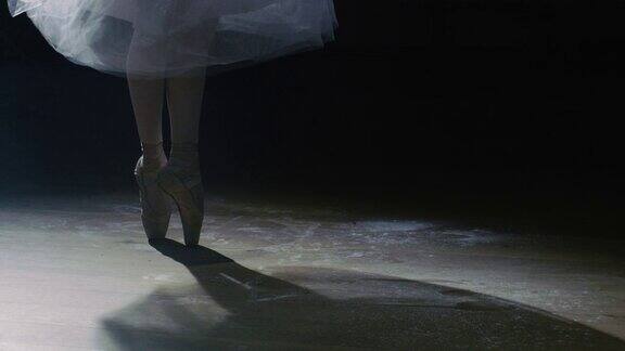 特写镜头的芭蕾舞女演员的腿在黑暗中她穿着芭蕾舞鞋在聚光灯下跳舞她穿着白色芭蕾舞裙”在缓慢的运动