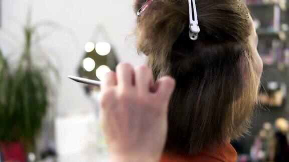 美发师在美容院用电熨斗为坐着的女士拉直头发她手里拿着一种特殊的器械轻轻地从上到下在短短的金发上移动