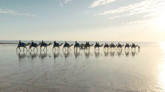 游客们在日落时分骑着骆驼沿着布鲁姆的电缆海滩出发