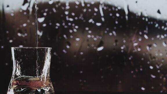 将威士忌倒入玻璃杯中特写在窗外的雨中倒着威士忌
