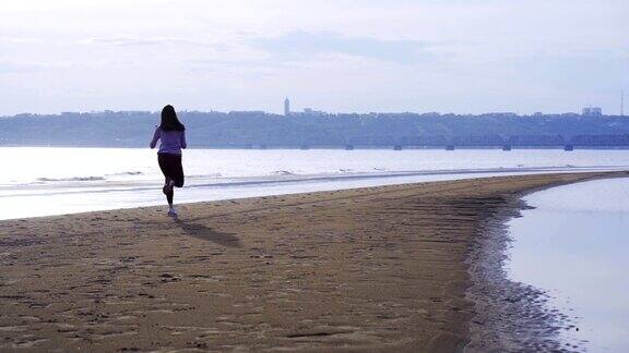 一个夏天的早晨穿着运动服的年轻苗条的黑发女子沿着沙滩跑步