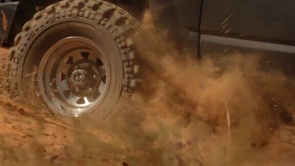 车轮的特写一辆越野车在沙漠上爬坡扬起灰尘的云侧视汽车在越野路上向上坡行驶