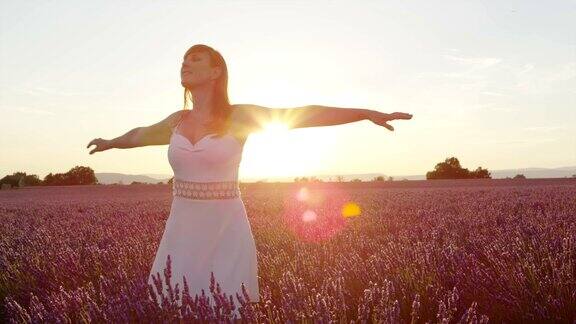 慢镜头:在金色的夕阳下一个快乐的年轻女子在美丽的紫色和淡紫色的田野中旋转